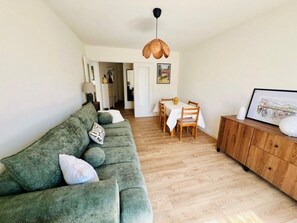 A living room with a green sofa, wooden dining table, and a hanging light fixture. - Apartment with garage, pets allowed - 4 guests (Amélie-les-Bains-Palalda)