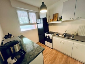 A compact kitchen with a gas stove, a refrigerator, a sink, and a window with curtains. - Apartment with garage, pets allowed - 4 guests (Amélie-les-Bains-Palalda)