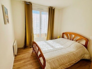 A bedroom with a wooden bed frame, a window with curtains, and a radiator on the wall. - Apartment with garage, pets allowed - 4 guests (Amélie-les-Bains-Palalda)