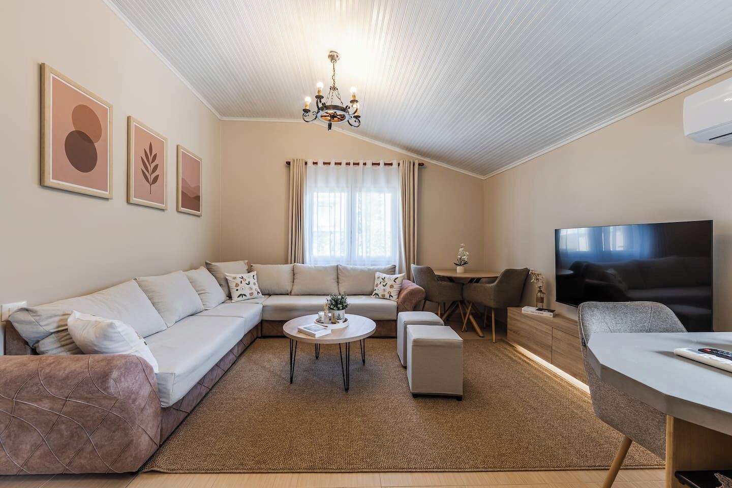 Ein modernes Wohnzimmer mit einem Ecksofa, einem runden Couchtisch, einem Fernseher und einem Essbereich.