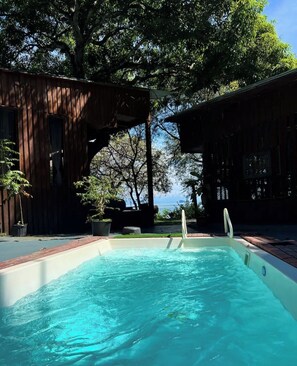 A swimming pool with a wooden deck, surrounded by trees and a view of the sea. - Unique and private rustic villa (Paquera)
