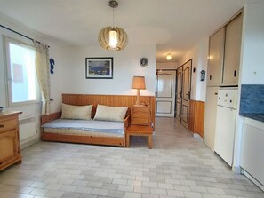 A room with a bed, a desk, a lamp, a refrigerator, and a kitchen area. - T2 Cabin Apartment - 35m² - Saint-Pierre-La-Mer (Fleury-Saint-Pierre-la-Mer)