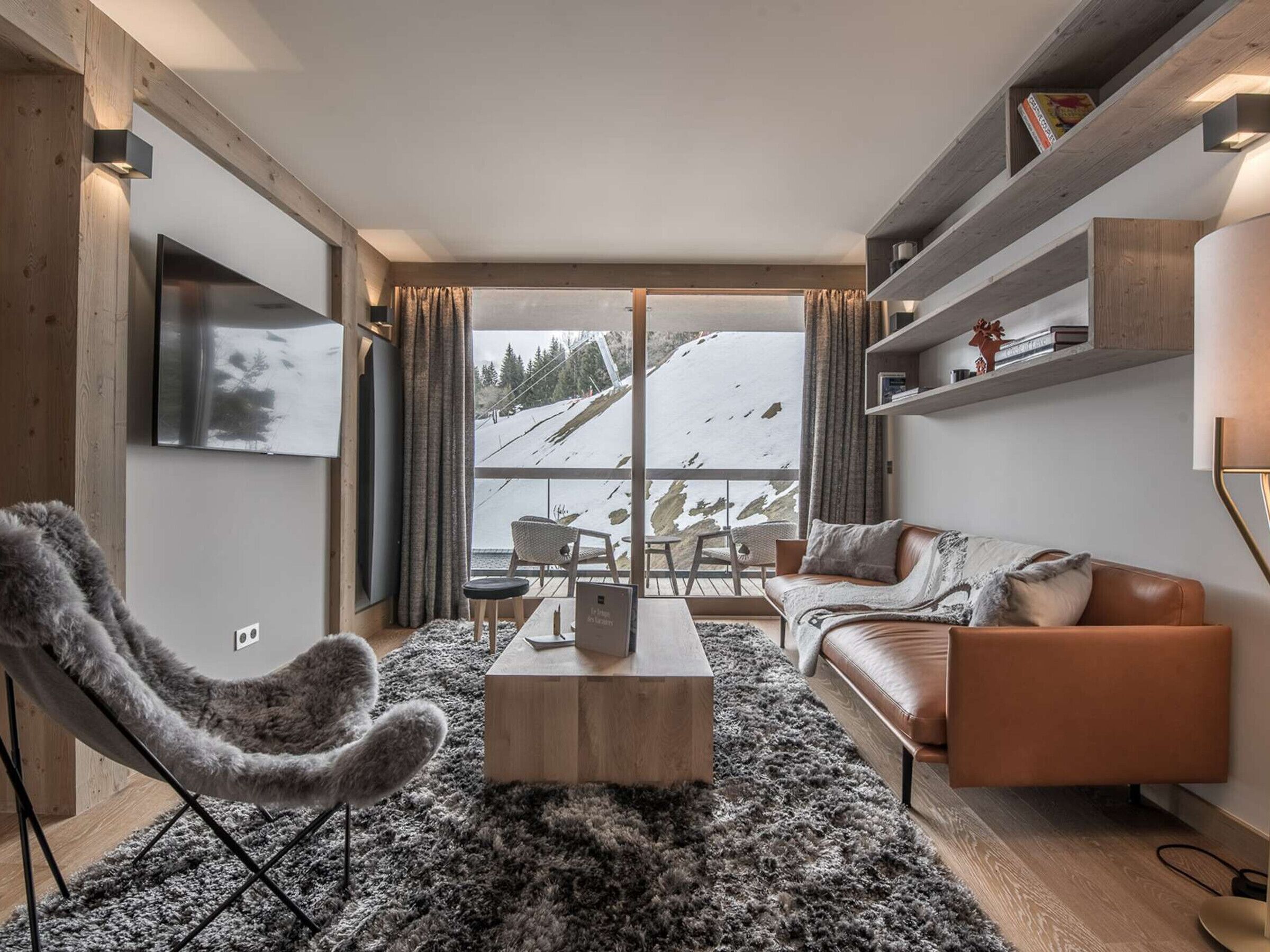 A modern living room with a sofa, armchair, coffee table, and a view of a snowy landscape.