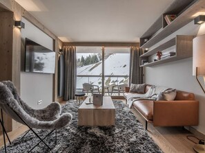 Ein modernes Wohnzimmer mit Sofa, Sessel, Couchtisch und Blick auf eine verschneite Landschaft.