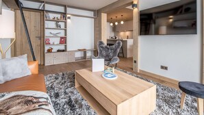 A modern living room with a sofa, a coffee table, a fireplace, and a kitchen in the background. - Stunning apartment in the center - 8 guests (Courchevel 1550)