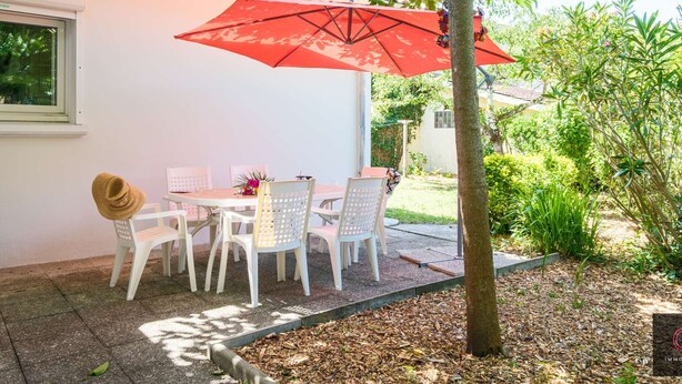 An outdoor patio with a table and chairs, a red umbrella, and a tree. - Family home in the city center - 8 guests (Biscarrosse)