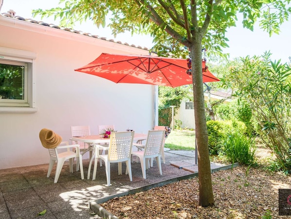 An outdoor patio with a table and chairs, a red umbrella, and a tree. - Family home in the city center - 8 guests (Biscarrosse)
