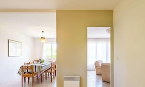 A dining area with a table set for four, a hanging light fixture, and a view through an open doorway to a living area with a sofa. - Family home in the city center - 8 guests (Biscarrosse)