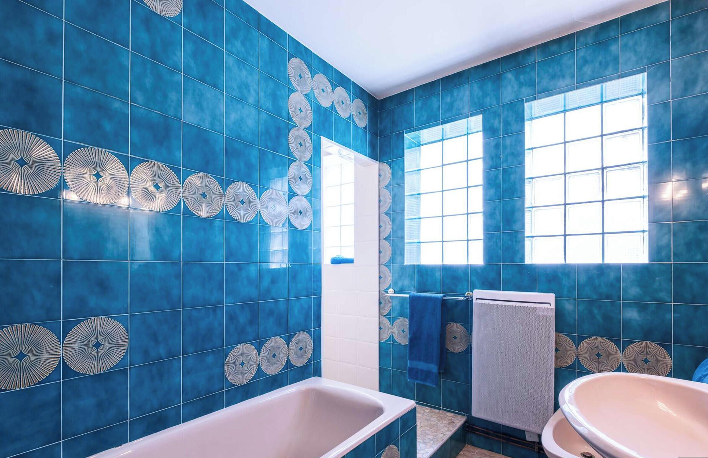 A bathroom with blue tiles, a bathtub, a sink, and a window.