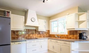A kitchen with white cabinets, a Bosch dishwasher, a clock, and a window with a view of trees. - Family home in the city center - 8 guests (Biscarrosse)
