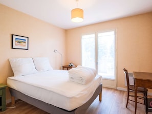 A bedroom with a bed, a desk, a chair, a lamp, and a window. - Family home in the city center - 8 guests (Biscarrosse)