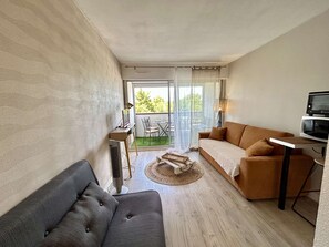 Ein modernes Wohnzimmer mit Sofa, einem kleinen Tisch, einem Fernseher und einem Balkon mit Gartenmöbeln.