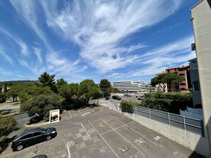 Ein Parkplatz mit markierten Stellplätzen, ein Gebäude im Hintergrund und Bäume.