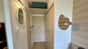 Un corridoio con pavimento in legno, uno specchio, una porta e un pannello di legno fissato al muro.