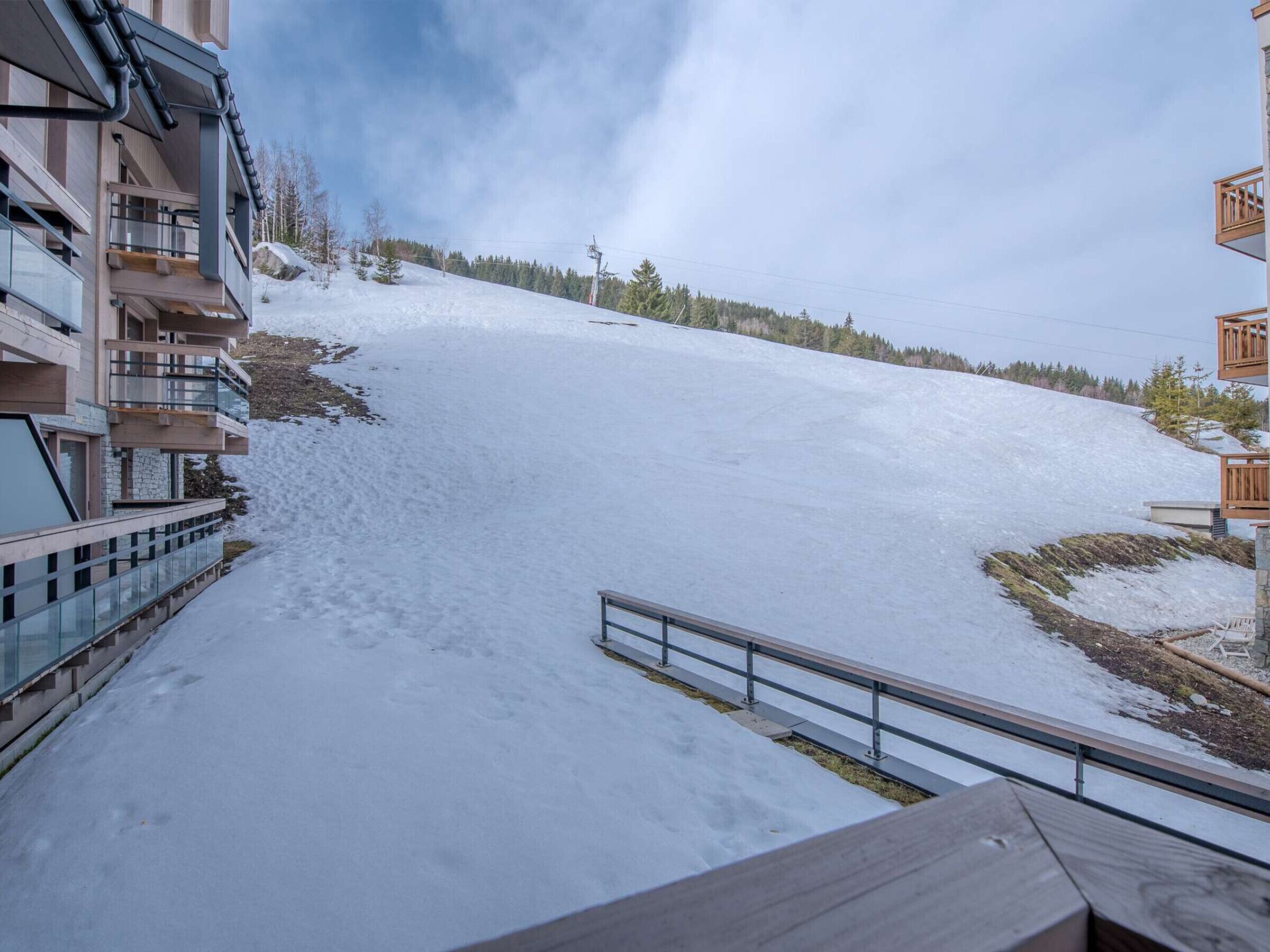 A snow-covered slope with a building on the left and a wooden structure on the right.