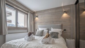 Ein Schlafzimmer mit einem großen Bett, Holzwandverkleidung, einem Fenster mit Vorhängen und einem Nachttisch.