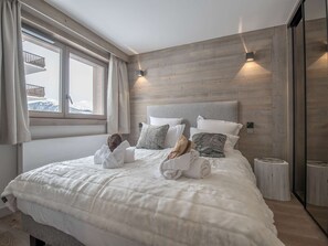 Ein Schlafzimmer mit einem großen Bett, Holzwandverkleidung, einem Fenster mit Vorhängen und einem Nachttisch.