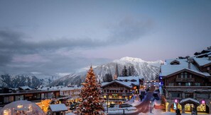 Eine verschneite Bergstadt mit einem markanten Weihnachtsbaum, Holzhäusern und einem gut sichtbaren Rolex-Geschäft.