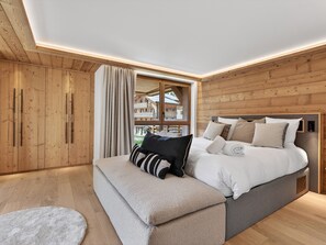 Ein Schlafzimmer mit Holzbalkendecke, einem großen Bett mit vielen Kissen, einer Bank und einem Fenster mit Vorhängen.