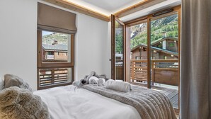 A bedroom with a large bed, a window with a view of a wooden cabin, and a sliding glass door. - Spacious apartment - 8 guests (Val-d'Isère)
