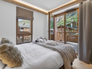 Ein Schlafzimmer mit einem großen Bett, einem Fenster mit Blick auf eine Holzhütte und einer Schiebeglastür.