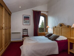 A bedroom with a bed, wooden headboard, a window with curtains, a chair, a nightstand, and a poster on the wall. - Cozy apartment in the center - 4 guests (Courchevel)