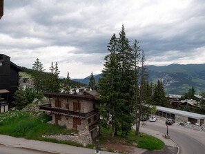 A mountain lodge with stone walls, a balcony, and a view of the surrounding mountains and valley. - Cozy apartment in the center - 4 guests (Courchevel)