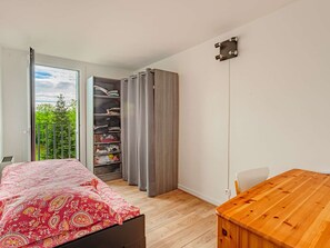 Une chambre à coucher avec un lit, une table en bois, une armoire et un balcon donnant sur un paysage verdoyant.