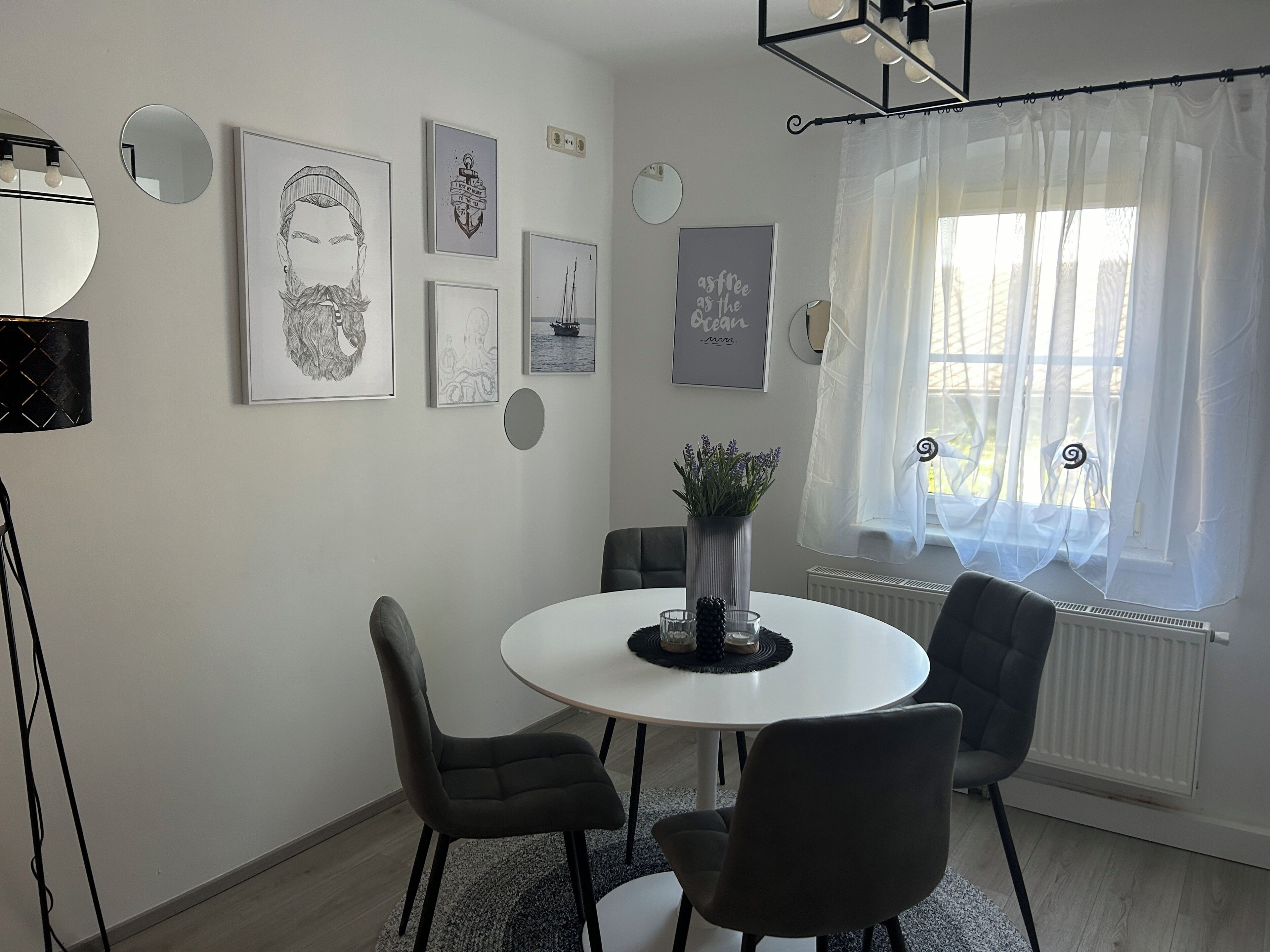 Een eethoek met een ronde tafel, vier stoelen, een bloemenvaas en wanddecoratie.