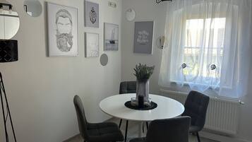 Een eethoek met een ronde tafel, vier stoelen, een bloemenvaas en wanddecoratie.