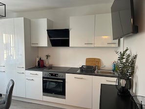 A modern kitchen with white cabinets, a black oven, a wooden cutting board, and a sink. - FarawayHomes Studios Schwertberg (Schwertberg)