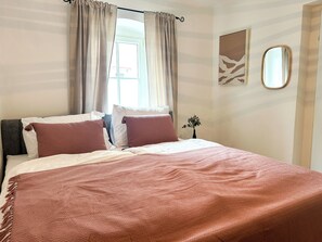 Hotellihuone, jossa on sänky, verhot, pieni kasvi ja peili seinällä.