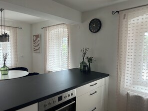 Una cocina moderna con encimera negra, armarios blancos, un reloj y objetos decorativos en el alféizar de la ventana.
