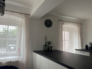 A kitchen with a black clock, a vase with flowers, and a coffee maker on the counter.