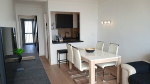 A modern living room with a dining table, chairs, a sofa, a TV, and a kitchen area. - Apartment sea view, AC - 4 guests (Canet-en-Roussillon)