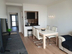 Ein modernes Wohnzimmer mit Esstisch, Stühlen, einer Couch, einem Fernseher und einer Küchenzeile.