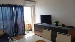 A modern living room with a flat-screen TV, a dining table, and a sofa. - Apartment sea view, AC - 4 guests (Canet-en-Roussillon)