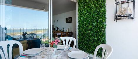 A dining area with a table set for four, a green wall, and a view of the sea.