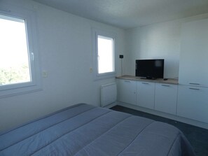 Ein Schlafzimmer mit einem Bett, einem Fernseher auf einem Schrank und zwei Fenstern.