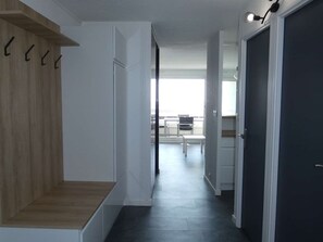 Ein Flur mit einer Holztreppe, weißen Wänden, einer dunklen Tür und Blick auf einen Essbereich mit Stühlen und einem Tisch.