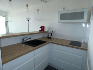 Eine moderne Küche mit einem schwarzen Spülbecken, einer Holz Arbeitsplatte, weißen Schränken, einem roten Wasserkocher und Pendelleuchten.