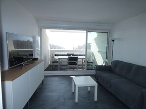 Ein modernes Wohnzimmer mit Flachbildfernseher, einer Couch, einem Couchtisch und einem Balkon mit Essbereich.