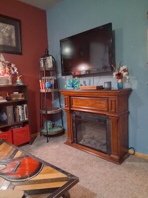 Ein Wohnzimmer mit Kamin, Fernseher, Bücherregal und Couchtisch.