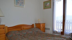 Une chambre à coucher avec un lit en bois, une table de chevet avec une lampe, une commode et une fenêtre avec des rideaux.