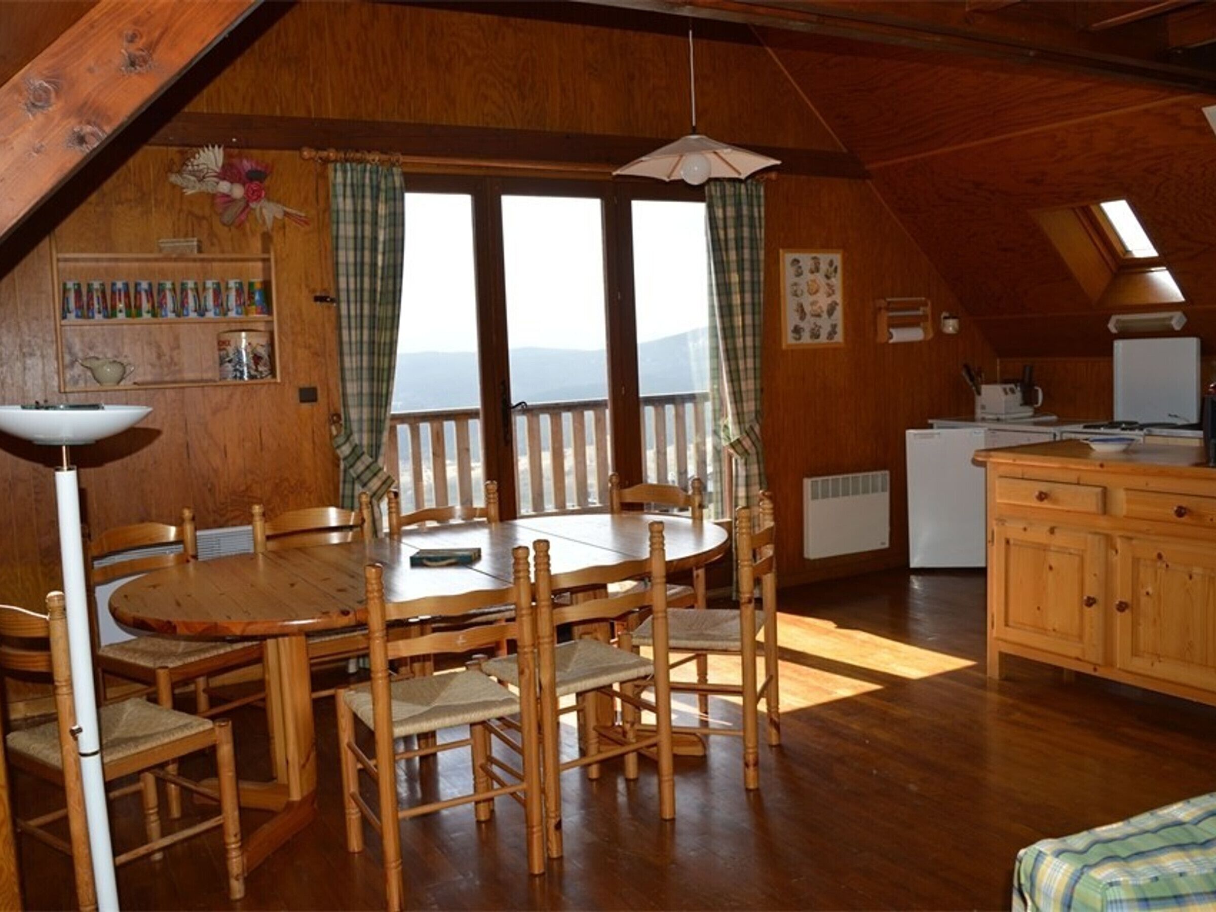 Un comedor acogedor de madera con mesa y sillas, una cocina con refrigerador y estufa, y un balcón con vistas.