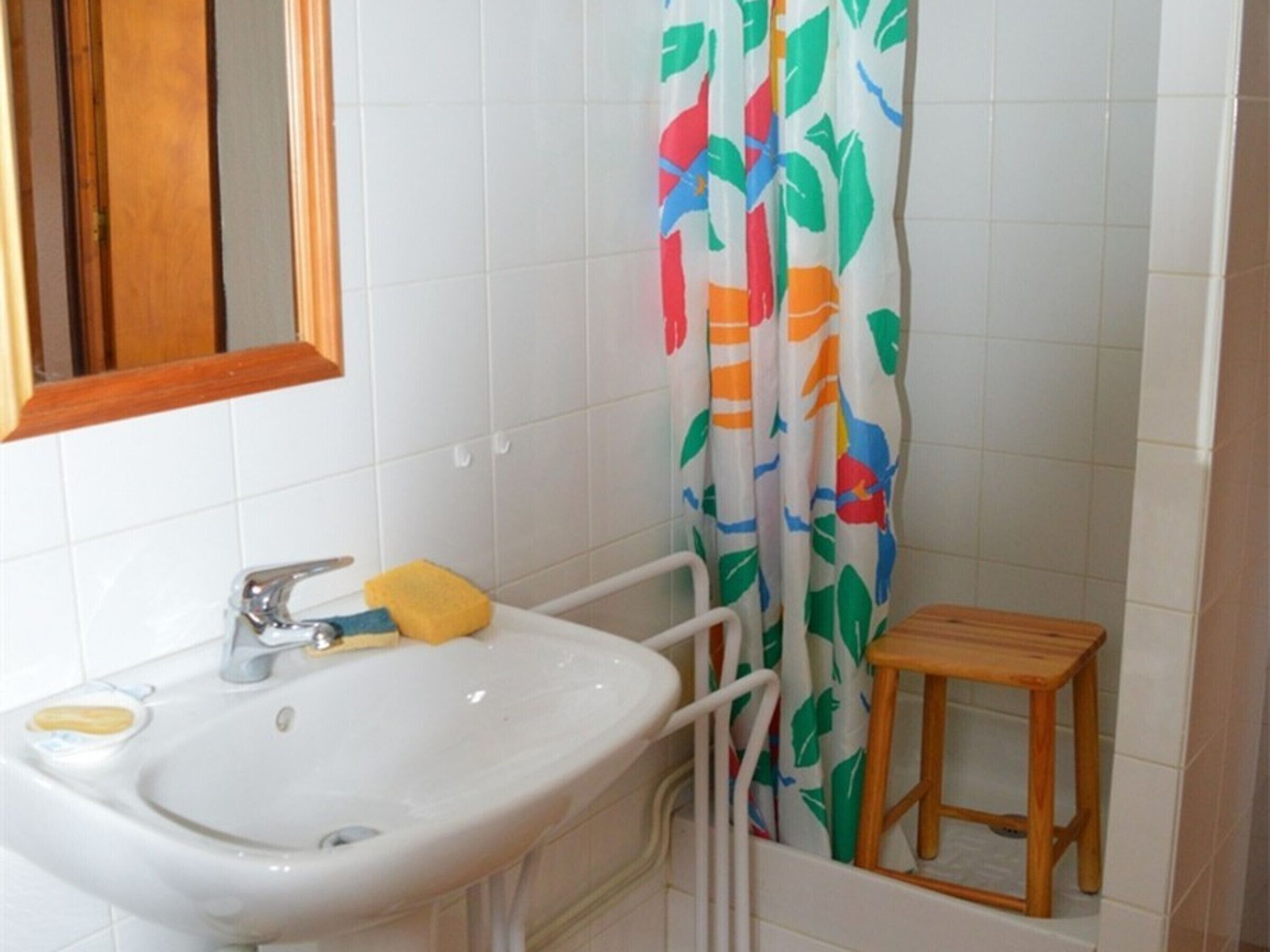 Un baño con lavamanos blanco, espejo y cortina de ducha con estampado de hojas de colores.