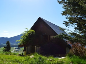 Eine Holzhütte mit geneigtem Dach, umgeben von üppiger Vegetation und einer Bergkulisse.