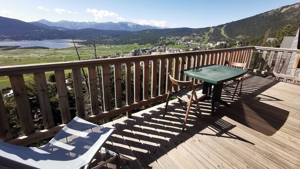 Une terrasse en bois avec une table et des chaises, offrant une vue sur un lac et des montagnes.