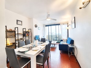 A dining area with a table set for four, a blue sofa, a ceiling fan, and a view through a large window. - Duplex Apartment for 6, Near Beach, Narbonne (Narbonne)