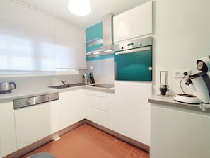 A compact kitchen with white cabinets, a built-in oven, a coffee machine, and a window with blinds. - Duplex Apartment for 6, Near Beach, Narbonne (Narbonne)